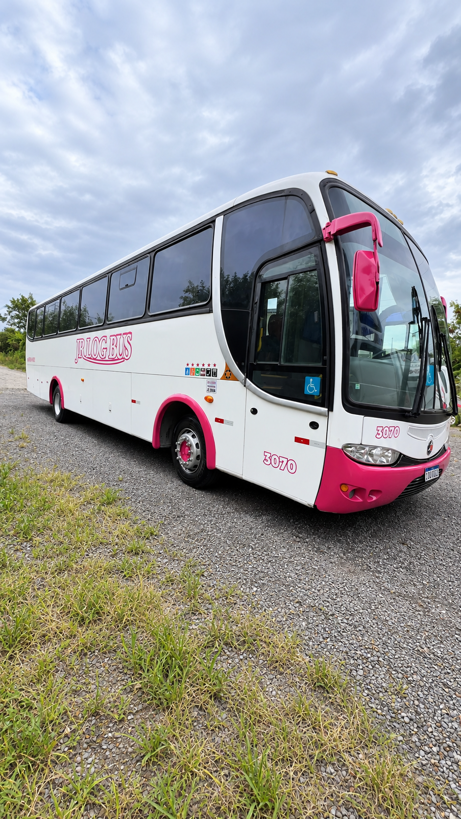Ônibus branco e rosa da JR Log Bus, em foto com cenário tratado